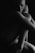 A black and white image of a nude person sitting curled up in a fetal position. Their face is partially visible, with the rest of the body mostly in shadow, creating a dramatic and intimate atmosphere. The lighting highlights the contours of the body, adding depth and emotion.