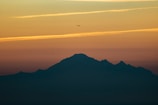 Sunset view of mountains with an airplane silhouette in the sky.
