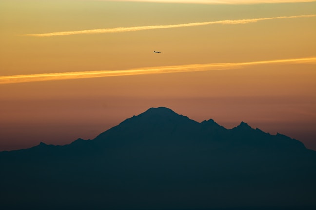 Sunset view of mountains with an airplane silhouette in the sky.