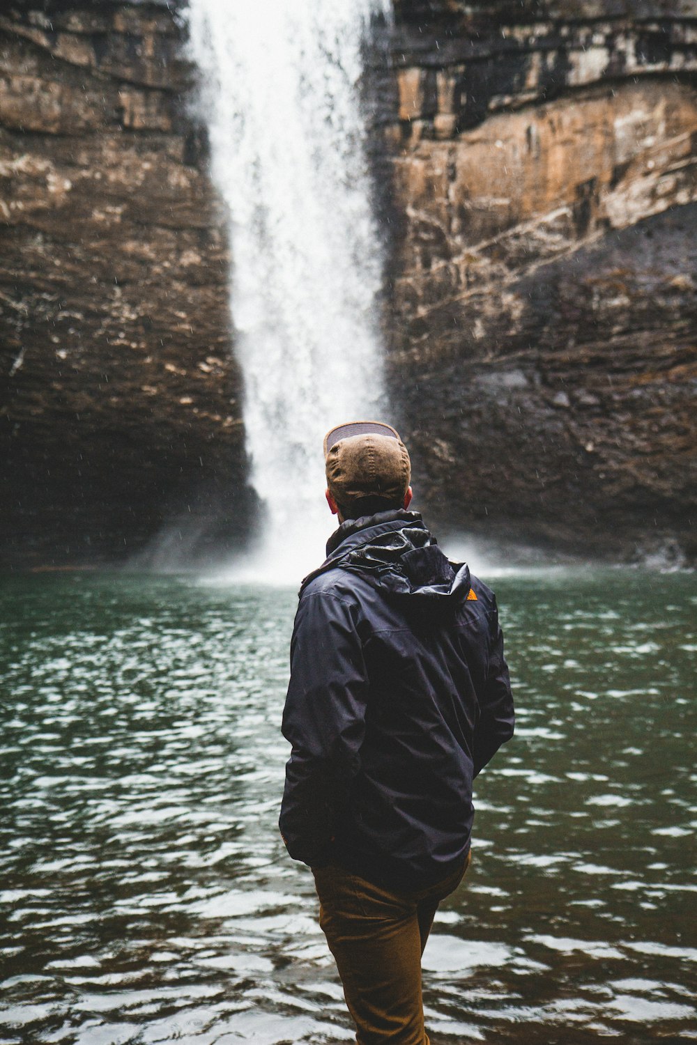 man wearing blue jacket standing near the waterfalls