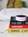 A small Amazon Echo device is placed on top of a stack of three books. The titles visible are 'Shoe Dog', 'Hacking Growth', and 'Humans', each with distinctive colors and fonts. The books are neatly stacked on a white surface, and in the background, a blurred, cozy-looking white and yellow pillow or blanket is visible.