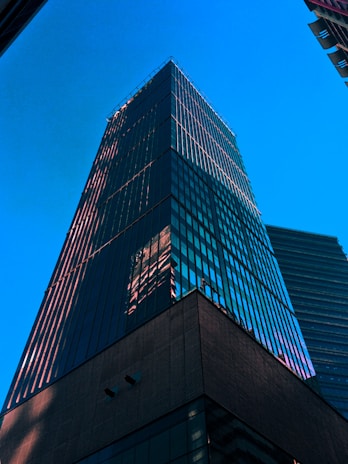 Close-up of a modern glass tower reflecting the surrounding urban landscape in daylight.