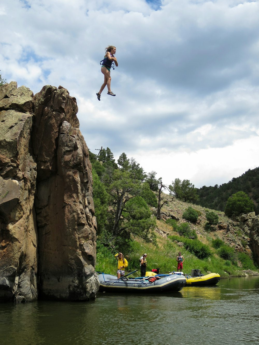 woman jumping from hill to body of water