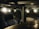 Dimly lit, dusty vintage cars are parked under a metal structure, with several lights illuminating the area. The scene appears to be a garage or storage space for classic vehicles, with a focus on the neglected and aged condition of the cars.