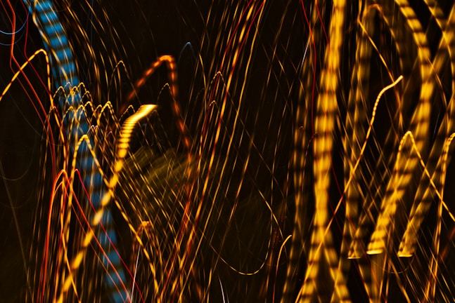 A dynamic display of abstract light patterns featuring swirling, elongated streaks of yellow, blue, and red against a dark background.