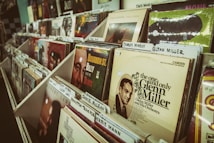 A collection of vinyl records is neatly arranged in a music store display. Various album covers are visible, featuring vintage designs and famous musicians like Glenn Miller, with organizer tabs labeling different artists.