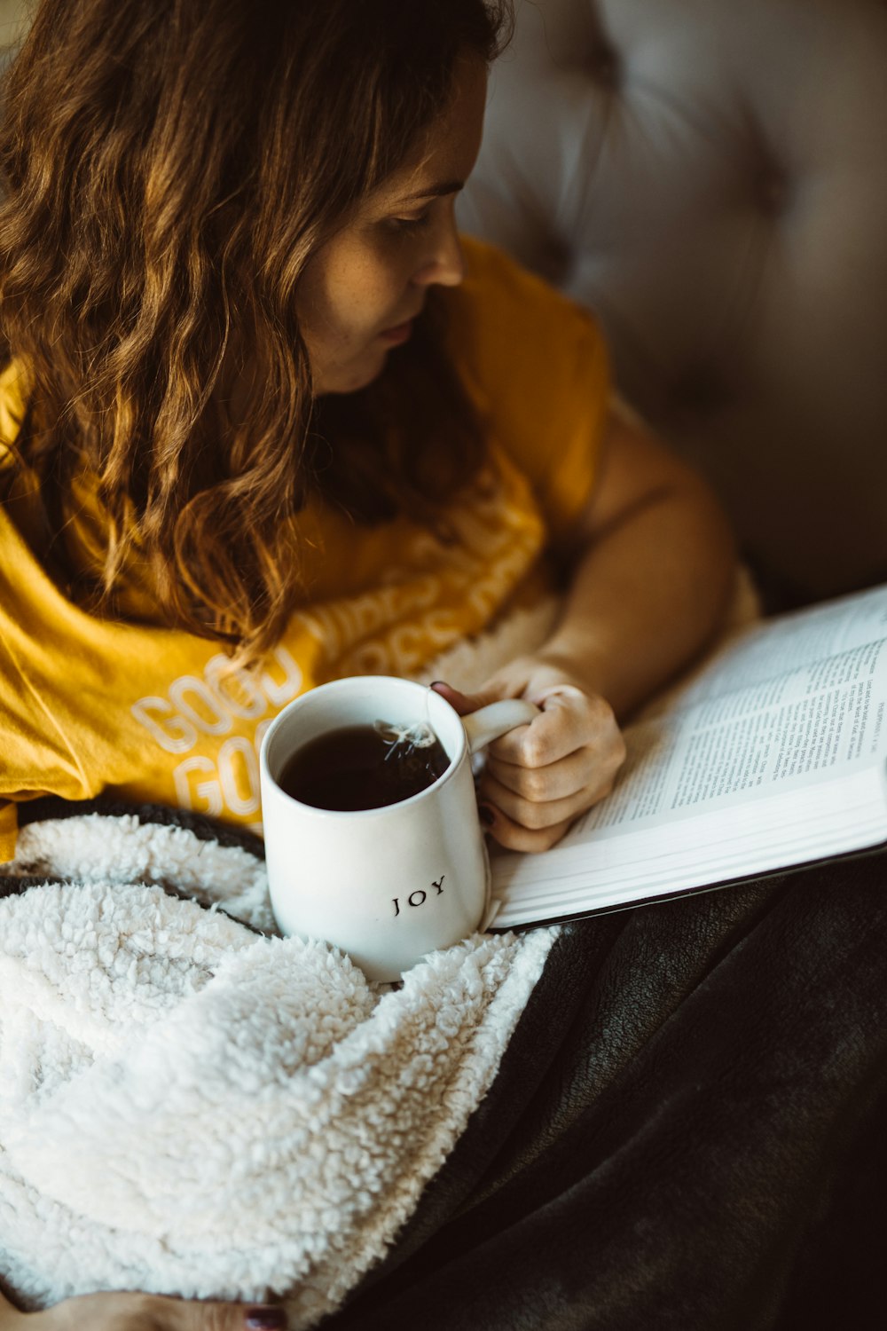 Frau liest Buch, während sie eine Tasse Kaffee hält
