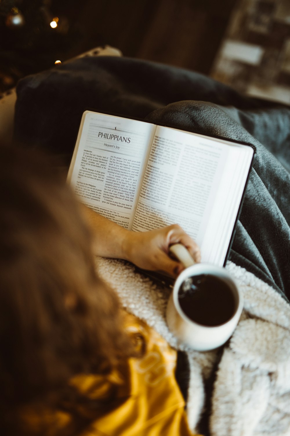 Persona sosteniendo una taza de cerámica blanca mientras lee un libro