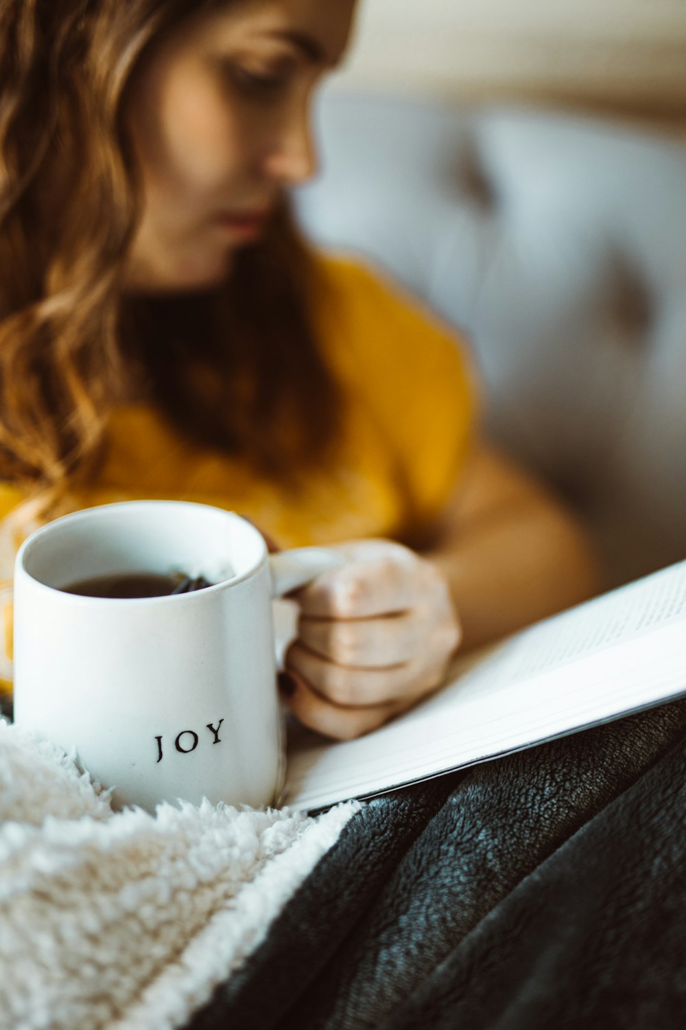 woman reading book holding white ceramic mug