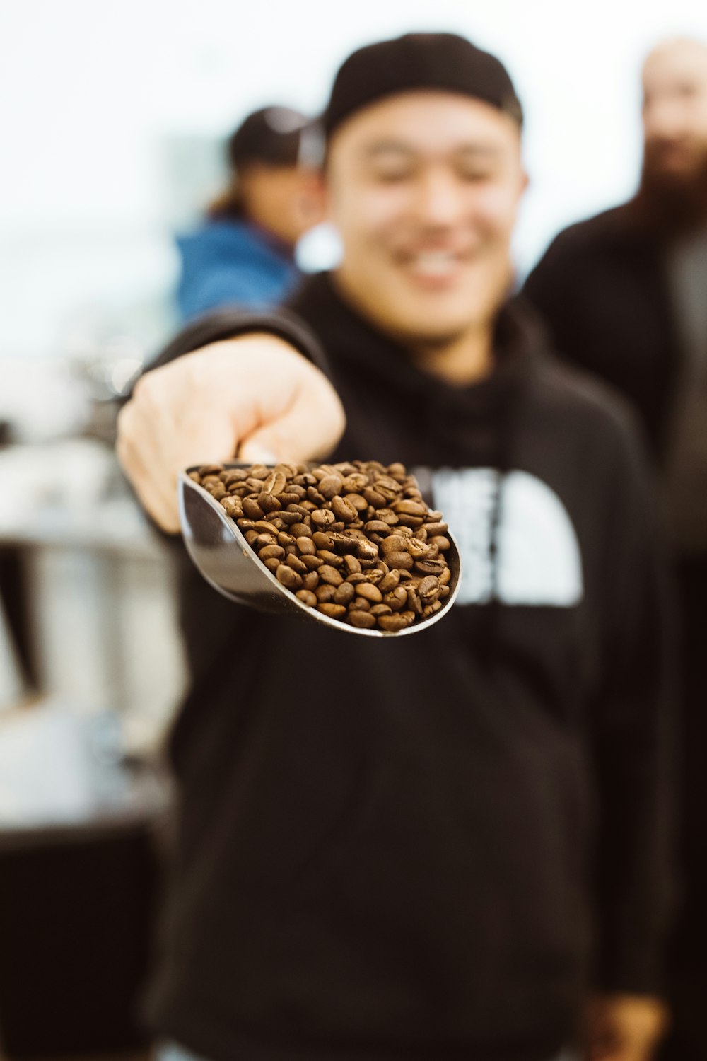 Mann im schwarzen Kapuzenpullover zeigt Schaufel Kaffeebohnen