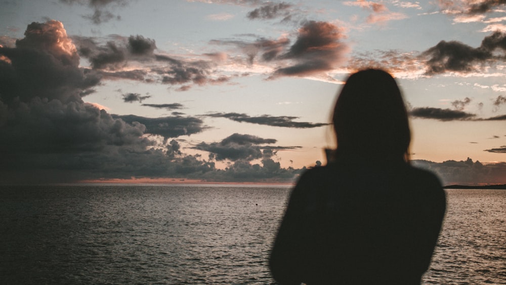 silhouette of woman standing on beach watching setting sun