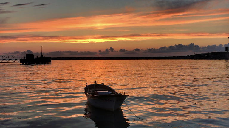 Golden sunset casting warm light over a wooden fishing boat anchored in the calm Po Delta lagoon