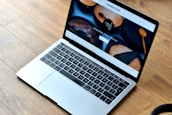 A sleek laptop with a silver body is open, displaying a webpage featuring wooden products. The wood-themed website includes images of handcrafted wooden items and text promoting their uniqueness and premium quality. The laptop rests on a wooden floor, complementing the aesthetic of the website displayed.