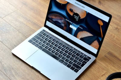 A sleek laptop with a silver body is open, displaying a webpage featuring wooden products. The wood-themed website includes images of handcrafted wooden items and text promoting their uniqueness and premium quality. The laptop rests on a wooden floor, complementing the aesthetic of the website displayed.