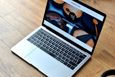 A sleek laptop with a silver body is open, displaying a webpage featuring wooden products. The wood-themed website includes images of handcrafted wooden items and text promoting their uniqueness and premium quality. The laptop rests on a wooden floor, complementing the aesthetic of the website displayed.