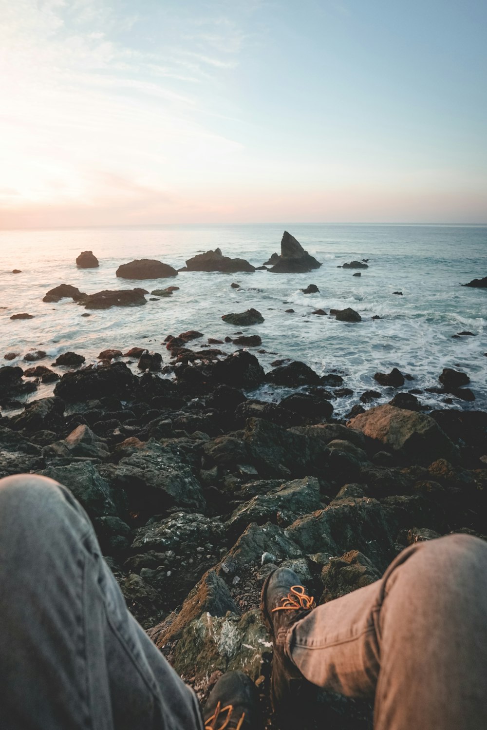 person sits on rocky beach facing setting sun