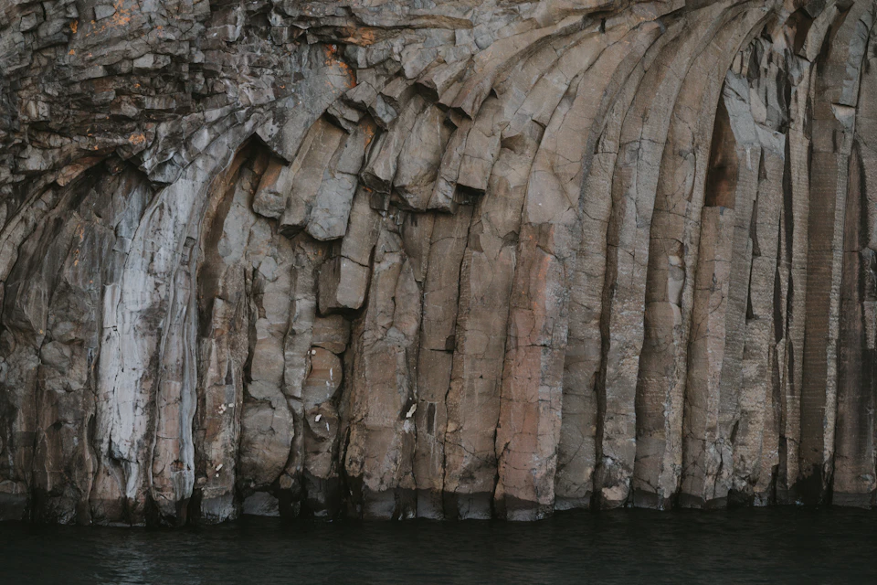 The image depicts a large, light brown rock formation with multiple layers and crevices. The rock is composed of numerous small rocks that have been worn away over time, creating a unique texture and pattern. The formation appears to be in a state of erosion or weathering, adding character to the scene. The perspective of the photo is from below, looking up at the towering presence of the rock formation.