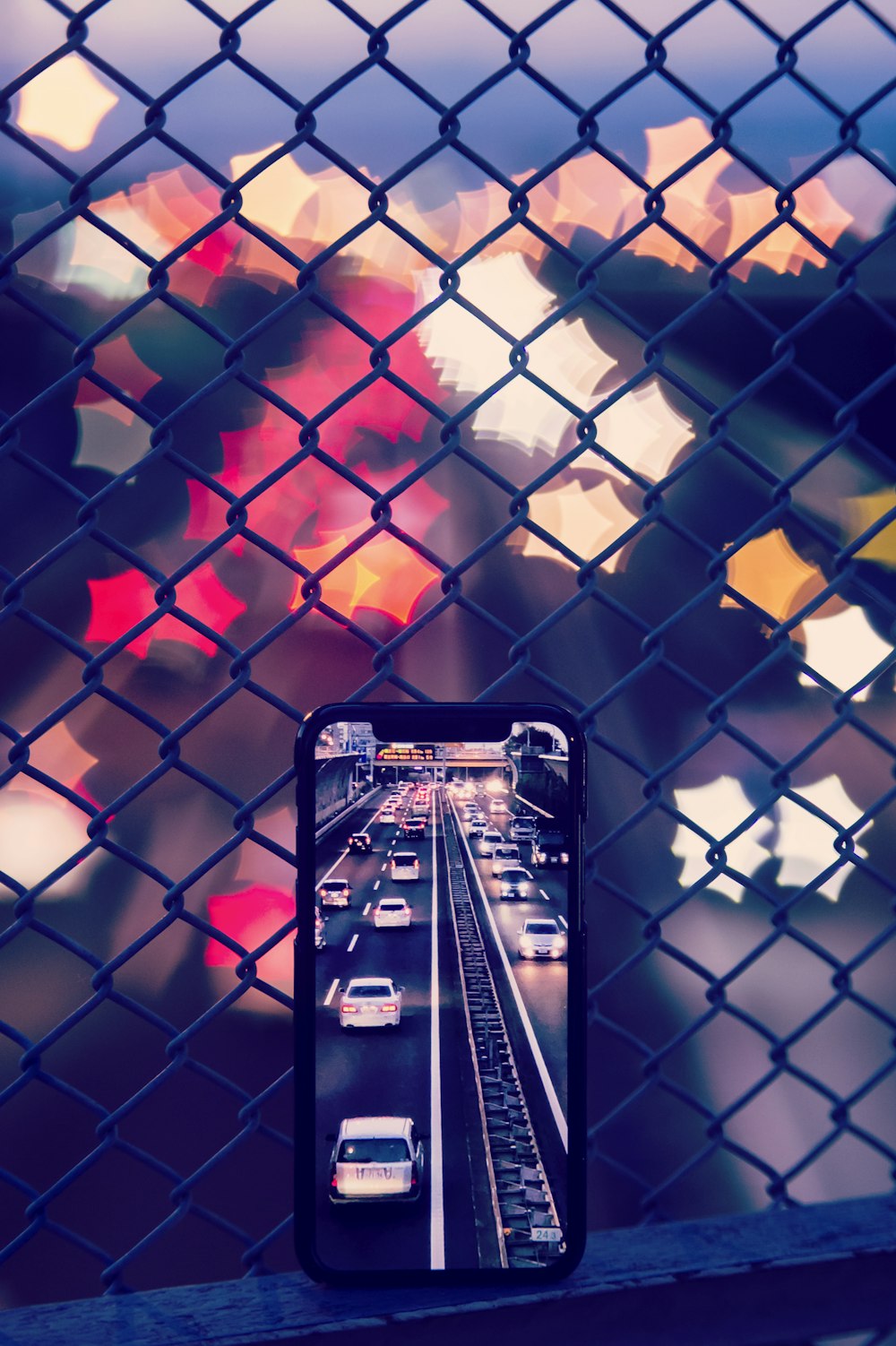 smartphone leaning on grey wired fence capturing vehicles on road