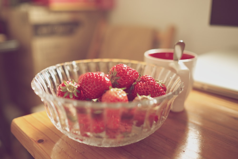 Schale mit Erdbeeren neben weißem Becher auf dem Tisch