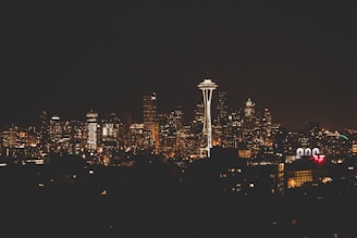 The city skyline at night is illuminated by numerous lights from the buildings, with the iconic Space Needle prominently standing out against the dark sky.