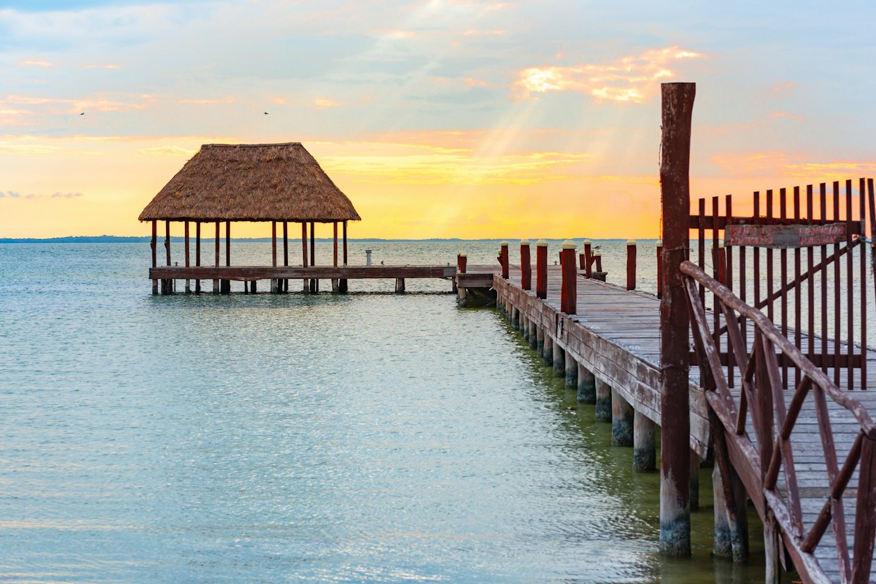 Wooden pier with a thatched palapa over calm water at sunset, one of the reasons Holbox is worth it for slow evenings