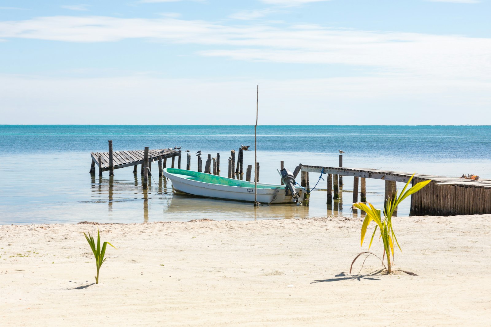 Small boat moored between weathered wooden docks on calm, clear water off a sandy Caye Caulker beach