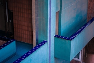 Geometric architecture with teal and blue hues is emphasized by stark, clean lines. Textured walls and sharp edges contrast with deep blue tiled accents. A combination of modern design and vivid color presents an almost abstract composition.
