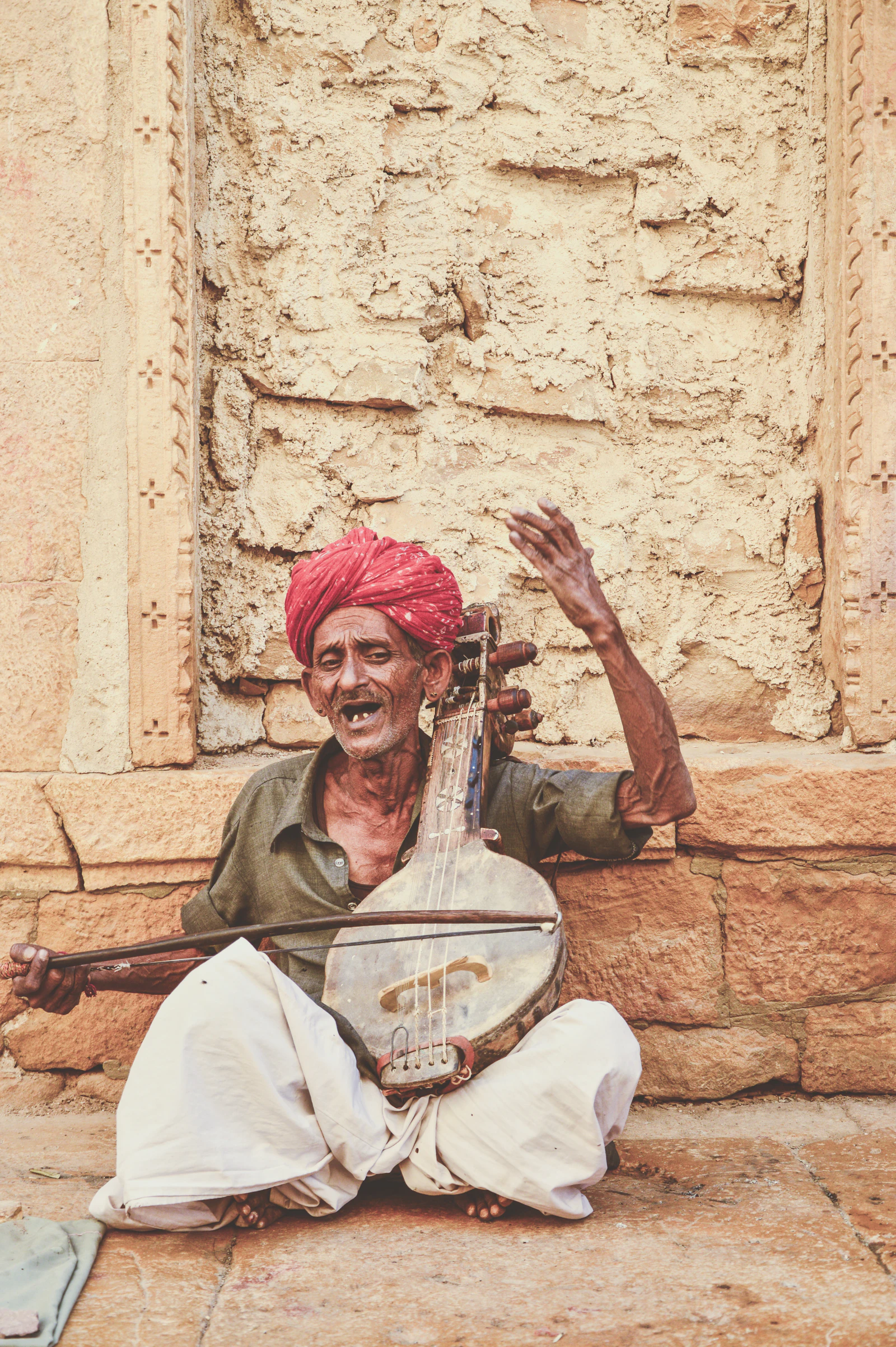 A musician seated on the floor playing a long-necked Indian string instrument