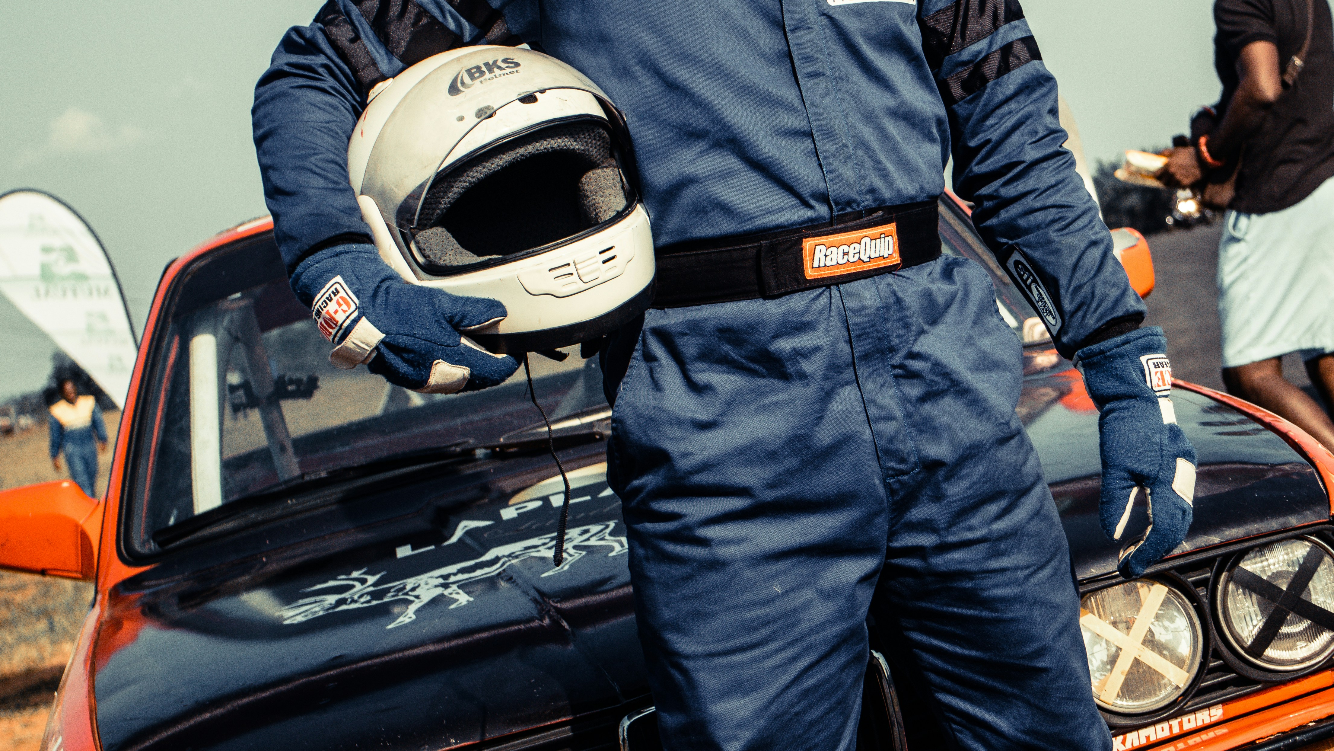 man in blue racing suit standing in front of blue coupe