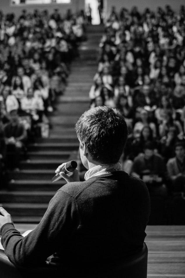 Black and white photo of a person speaking to a crowded auditorium