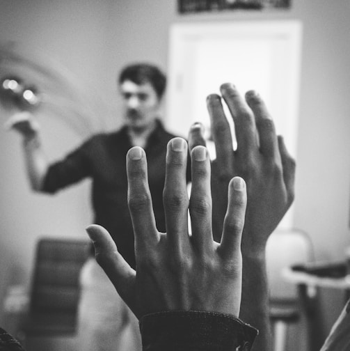 grayscale photography of two people raising their hands