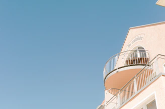A light peach-colored building with a semi-circular balcony framed by gray railings against a clear blue sky. The words 'Villa Brunhilde' are visible on the façade.
