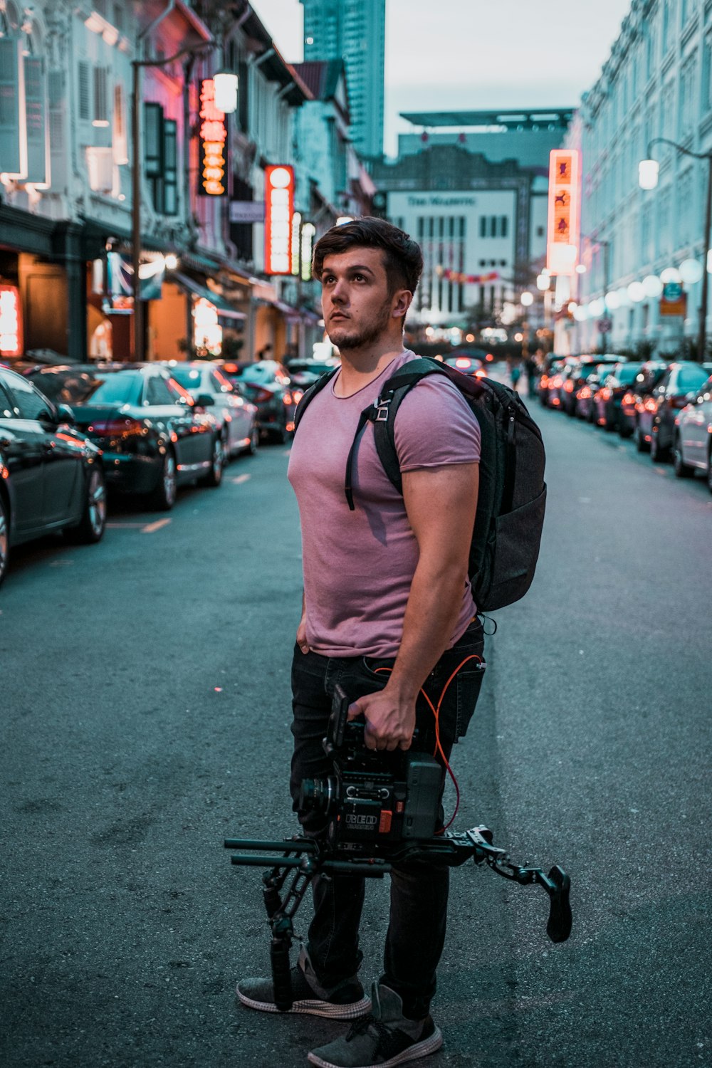 man holding camera standing on roadway between vehicles