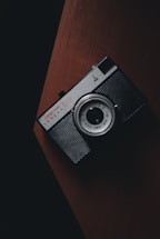 A moody, dark-themed photo of a camera resting on a wooden table with soft natural light highlighting its details.