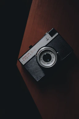 A moody, elegant photo of a vintage camera resting on a dark wooden table with soft, warm lighting.