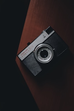 A moody, dark-themed photo of a camera resting on a wooden table with soft natural light highlighting its details.