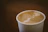 Close-up of a hand holding a Kagajkupa paper cup filled with steaming coffee.