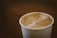 Close-up of a hand holding a Kagajkupa paper cup filled with steaming coffee.