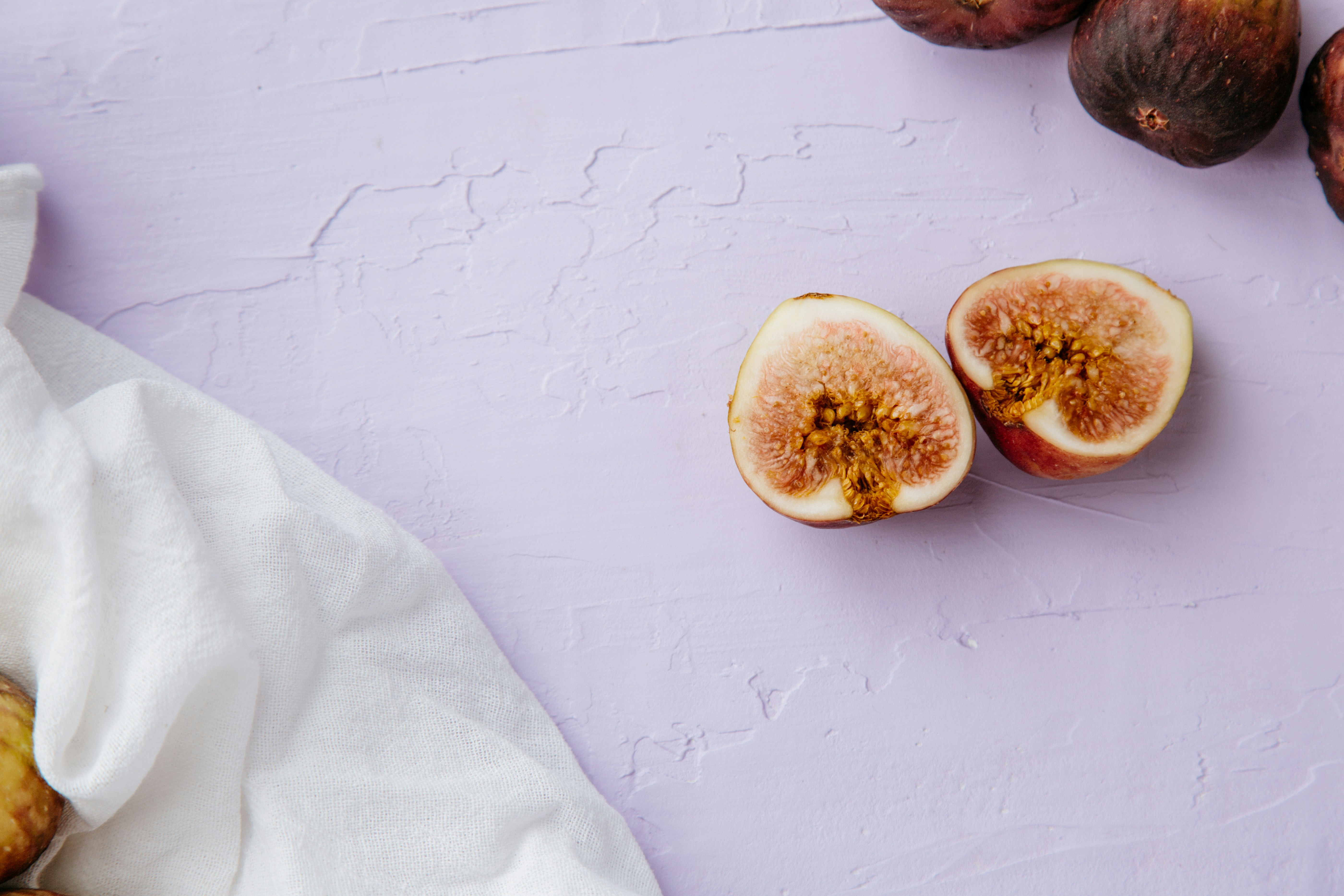 Gorgeous fresh fig halves against textured purple/lavender background with white linen. Great view of seeds and textures.