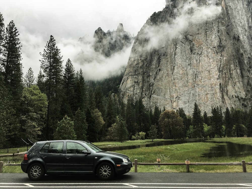 gray 5-door hatchback on the road near trees and mountain