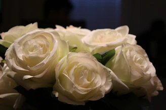 A close-up of an elegant bridal bouquet with white roses and greenery on a minimalist white background.
