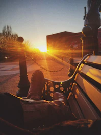 A close-up of rugged cowboy boots resting on a wooden fence under warm sunset light.