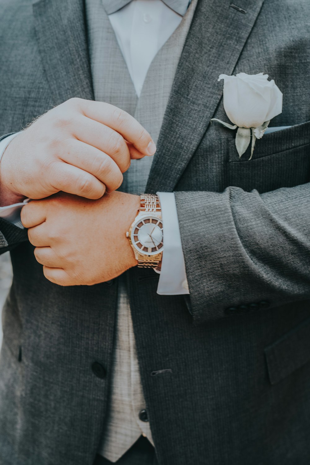 person wearing grey tuxedo and gold-colored watch with white rose brooch