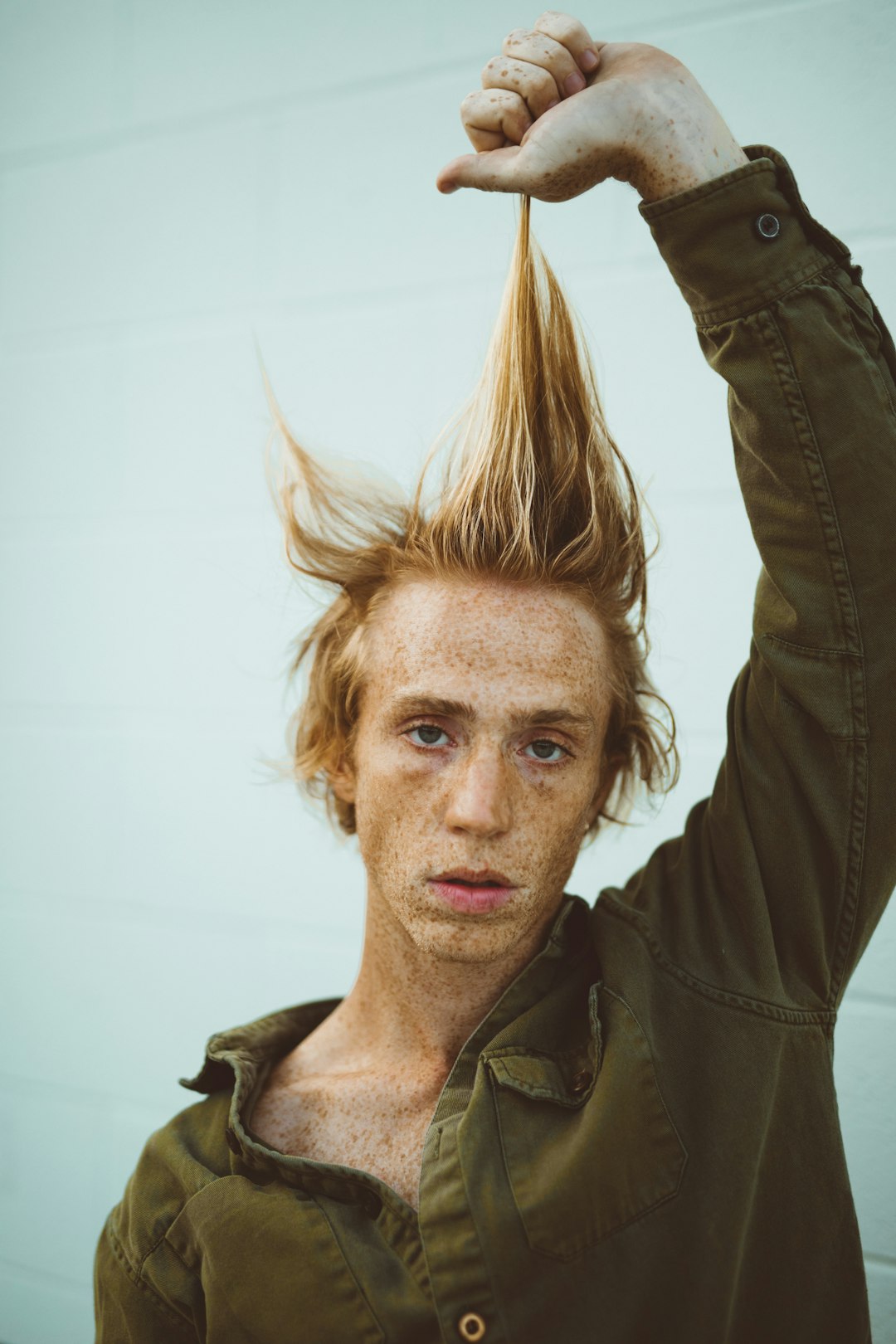 man pulling his hair up while standing near wall