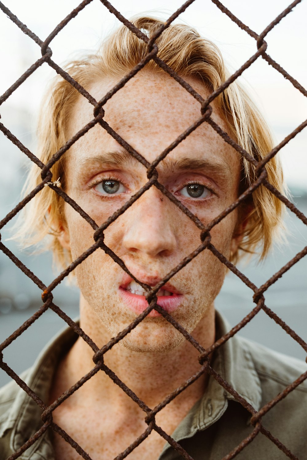 man in gray collared shirt standing behind chain link fence