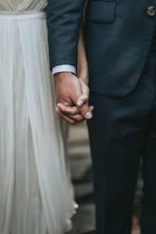 man in suit holding hands with woman in white skirt