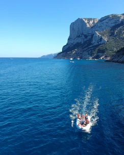 A sleek inflatable boat cruising near the rocky cliffs of Sella del Diavolo under a clear blue sky.