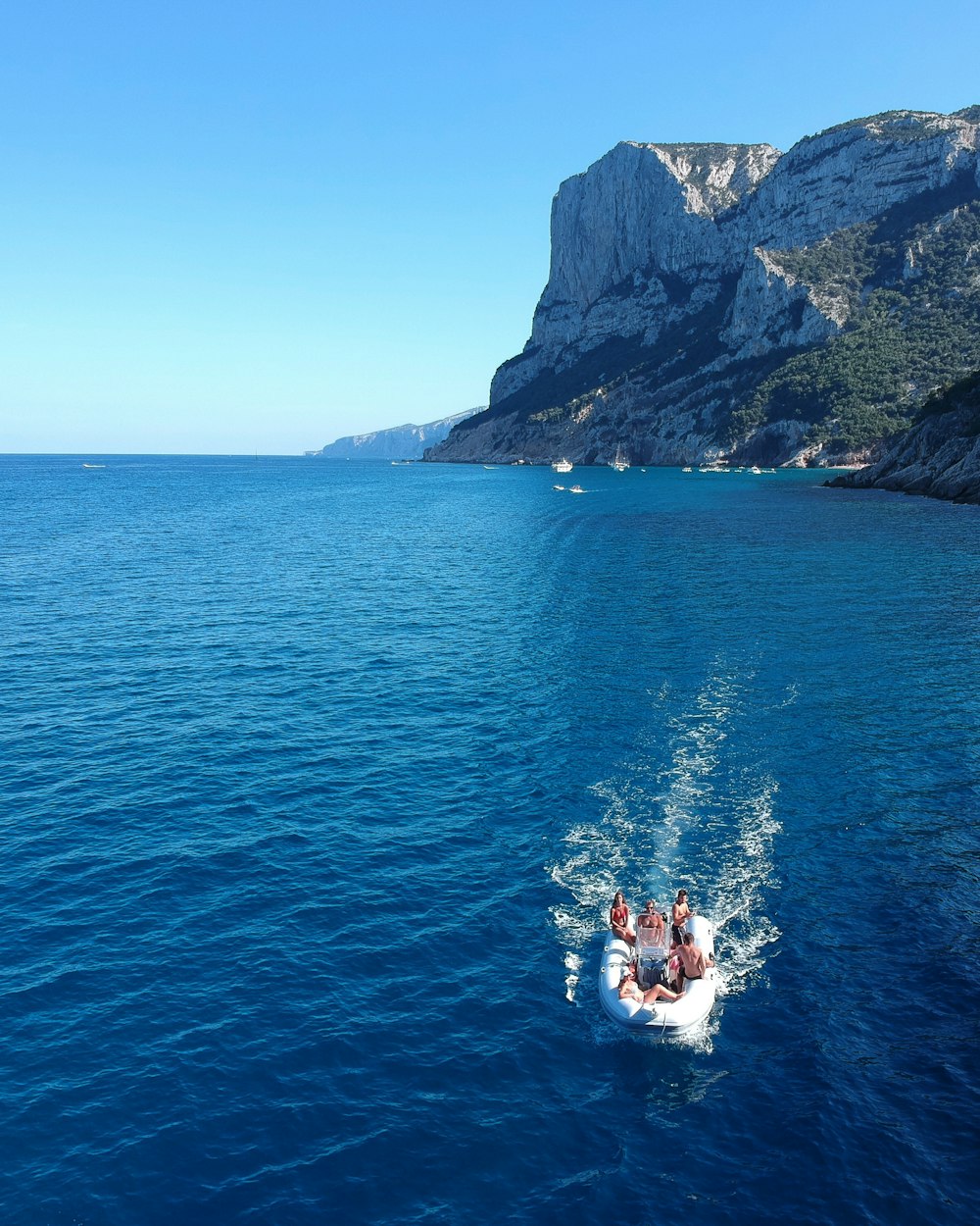 people in boat on body of water near cliff