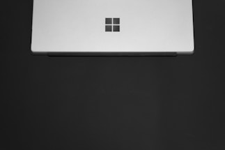 A sleek, silver laptop partially closed with a minimalist logo on the center of the lid. The laptop is set against a plain dark background, emphasizing its modern design.
