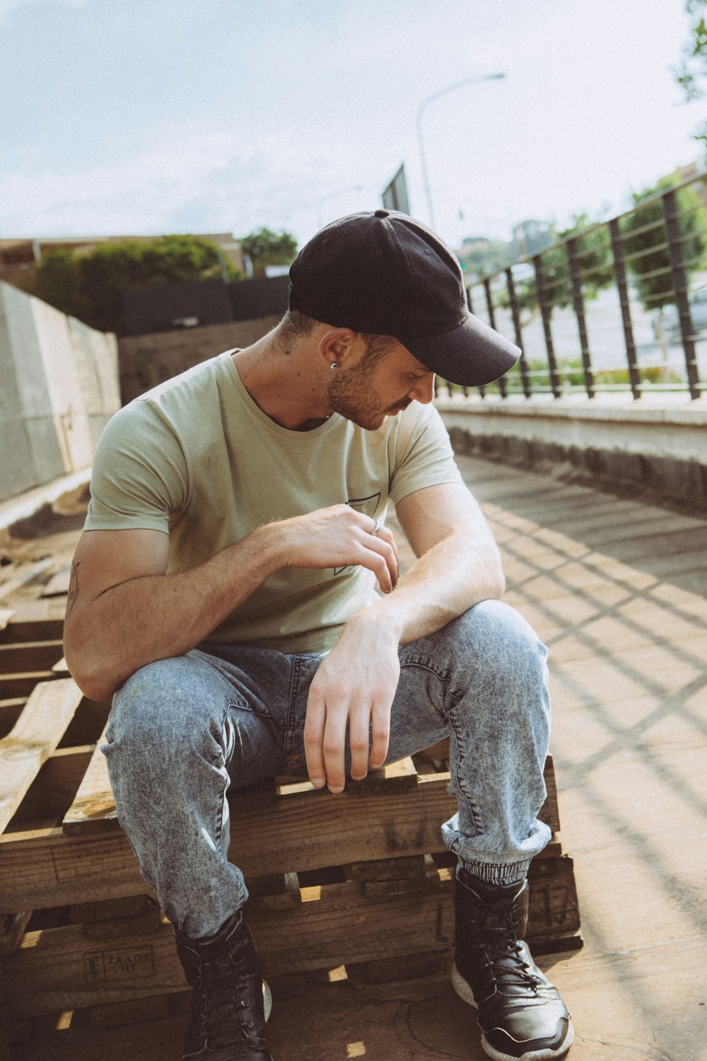 man sitting on wooden pallet looking at his shoulder downwards near handrail